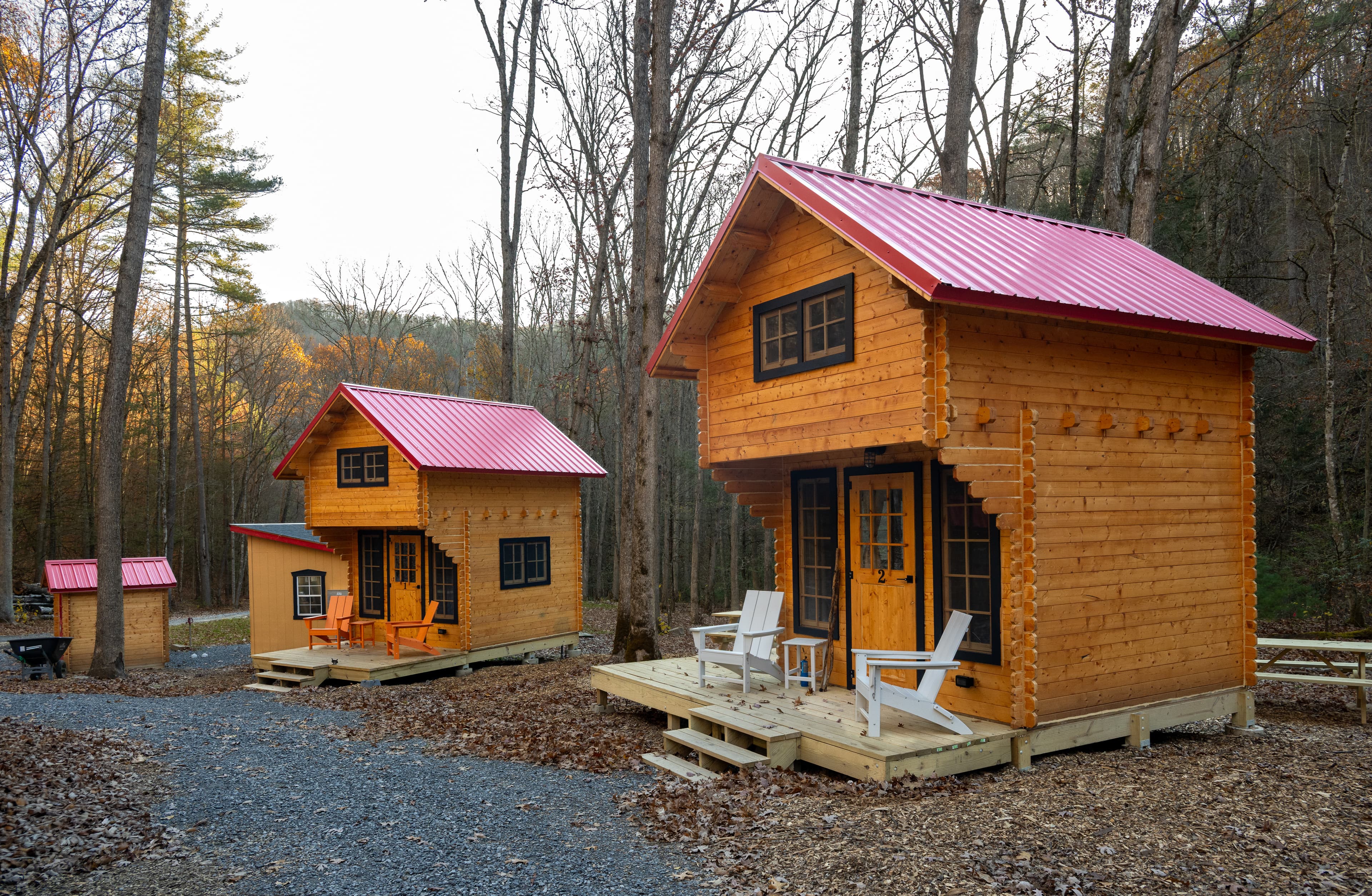 Two rustic wooden cabins with pink metal roofs surrounded by trees.
